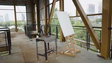 empty easel and art supplies on an industrial balcony overlooking a city