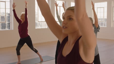 yoga class of healthy mature women practicing warrior pose enjoying morning physical fitness exercise workout in studio at sunrise