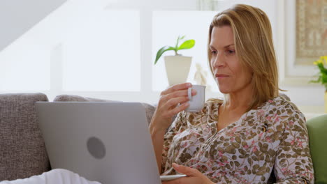mujer tomando café mientras usa una computadora portátil en el sofá 4k