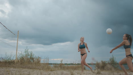 Mujeres-Jóvenes-Y-Hermosas-Están-Jugando-Voleibol-De-Playa-En-Un-Paisaje-Pintoresco-Con-Entrenamiento-Y-Competencia-De-Cielo-Nublado