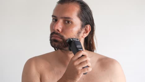 long haired man shaving with electric shaver