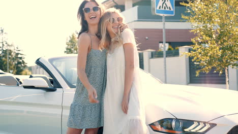 two women laughing beside a white convertible car