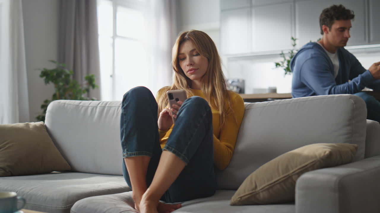 Internet addicted pair messaging smartphones at home. Woman scrolling cellphone