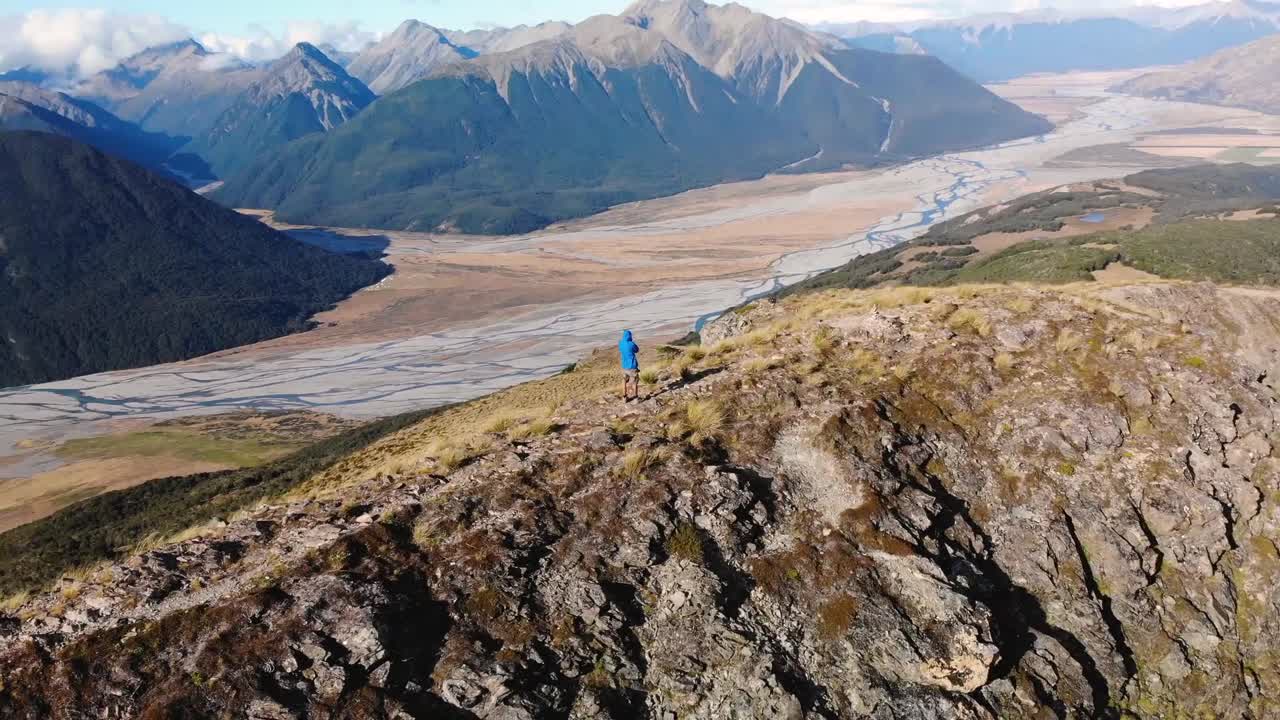 Man stands on ridge of high mountain aerial orbit shot. Reveal of beautiful Southern Alps landscape, New Zealand