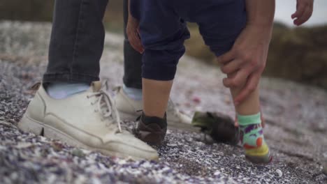 mom taking off the shoes and socks of her little girl at the beach - low-level shot