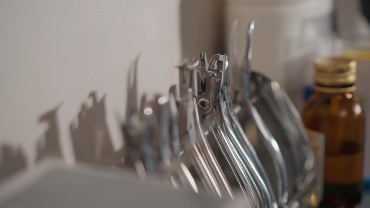 Close up of various metal orthodontic tools arranged on white surface in soft lighting. scene includes shiny metallic instruments with distinct shapes and sizes alongside blurred background