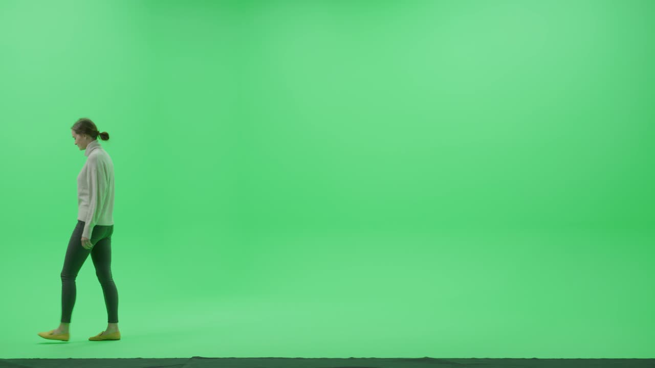 pantalla verde chroma clave estudio: hermosa mujer joven con ropa casual elegante camina a través de la habitación de derecha a izquierda. vista lateral disparada por la cámara