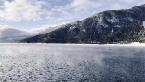 steam rising off the top of upper arrow lake with a landscape view of the mountains with alpine trees covered in snow