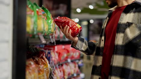 close up, a brunette man took a product from a supermarket counter and twirls it in his hands during inspection after which he returns it to its place