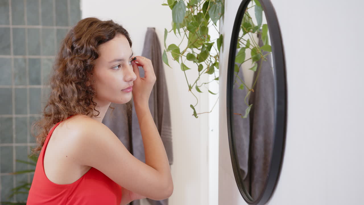 Donna che si trucca, guardandosi allo specchio in un ambiente domestico, rilassandosi.
