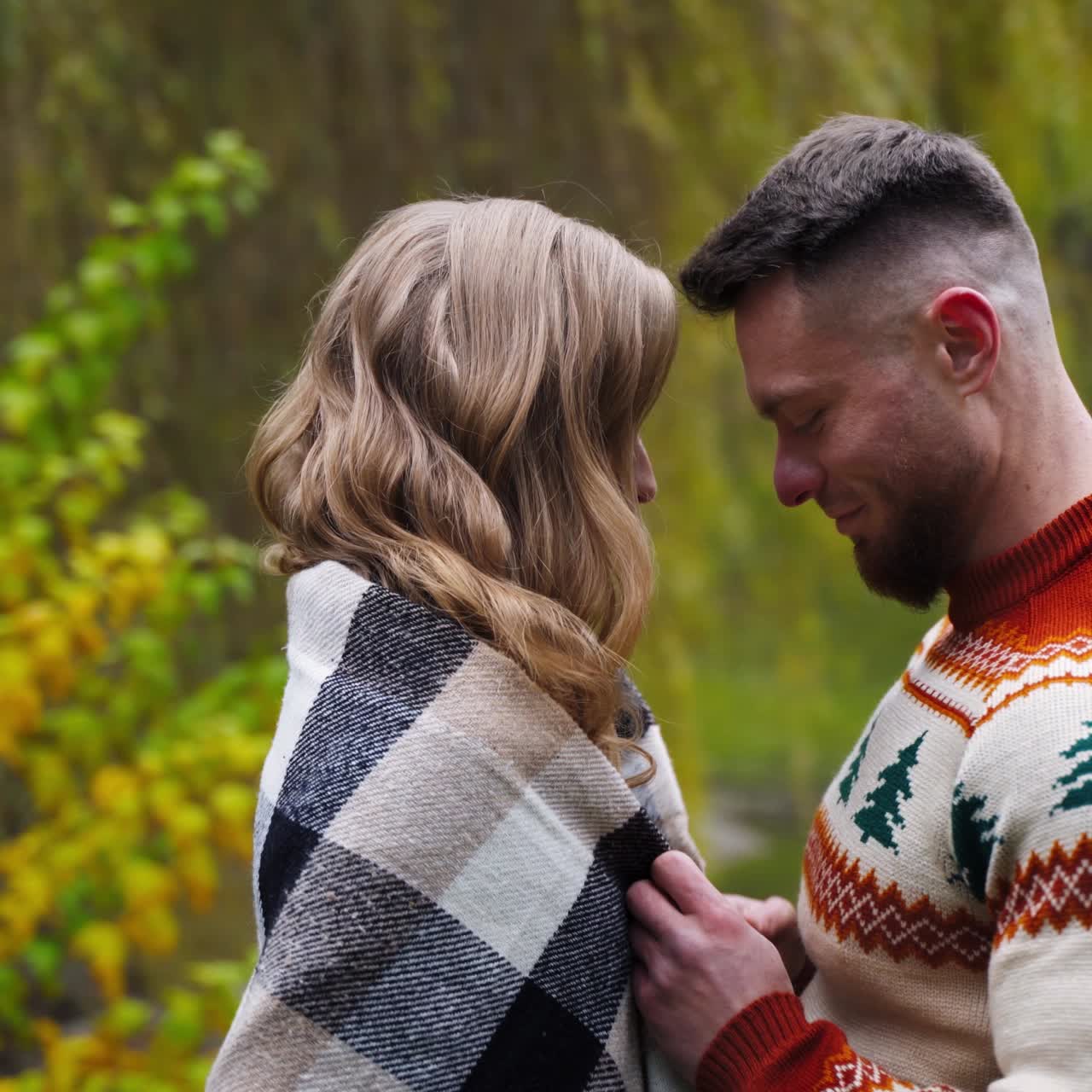Young man covered girl with blanket and hugged. Beautiful couple outside. Autumn nature background