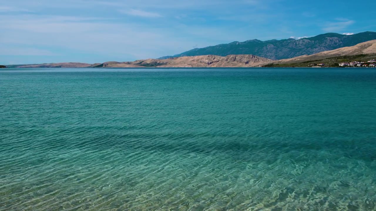 Ongerept transparant turquoise water van de baai van het eiland Pag met zachte golven, uitkijkend op het Velebit-gebergte