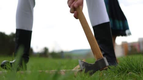 Young-Guy-Chops-Wood-with-Axe-in-Grass,-Low-Angle,-Close-Up