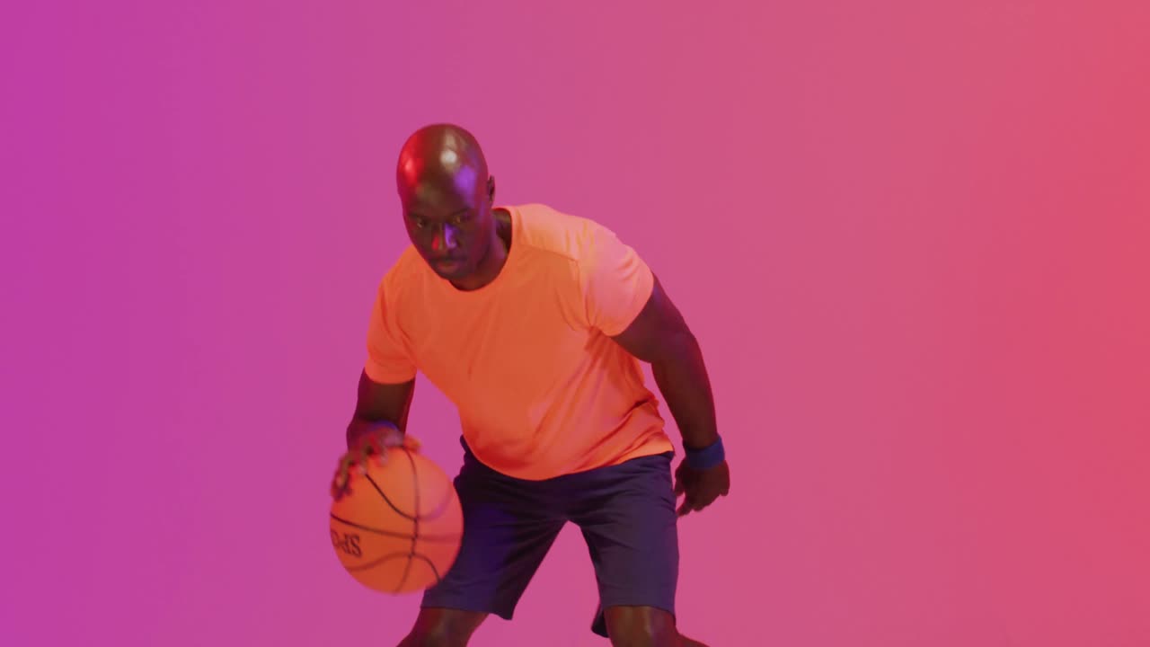 video de un jugador de baloncesto afroamericano rebotando la pelota sobre un fondo de color rosa a naranja