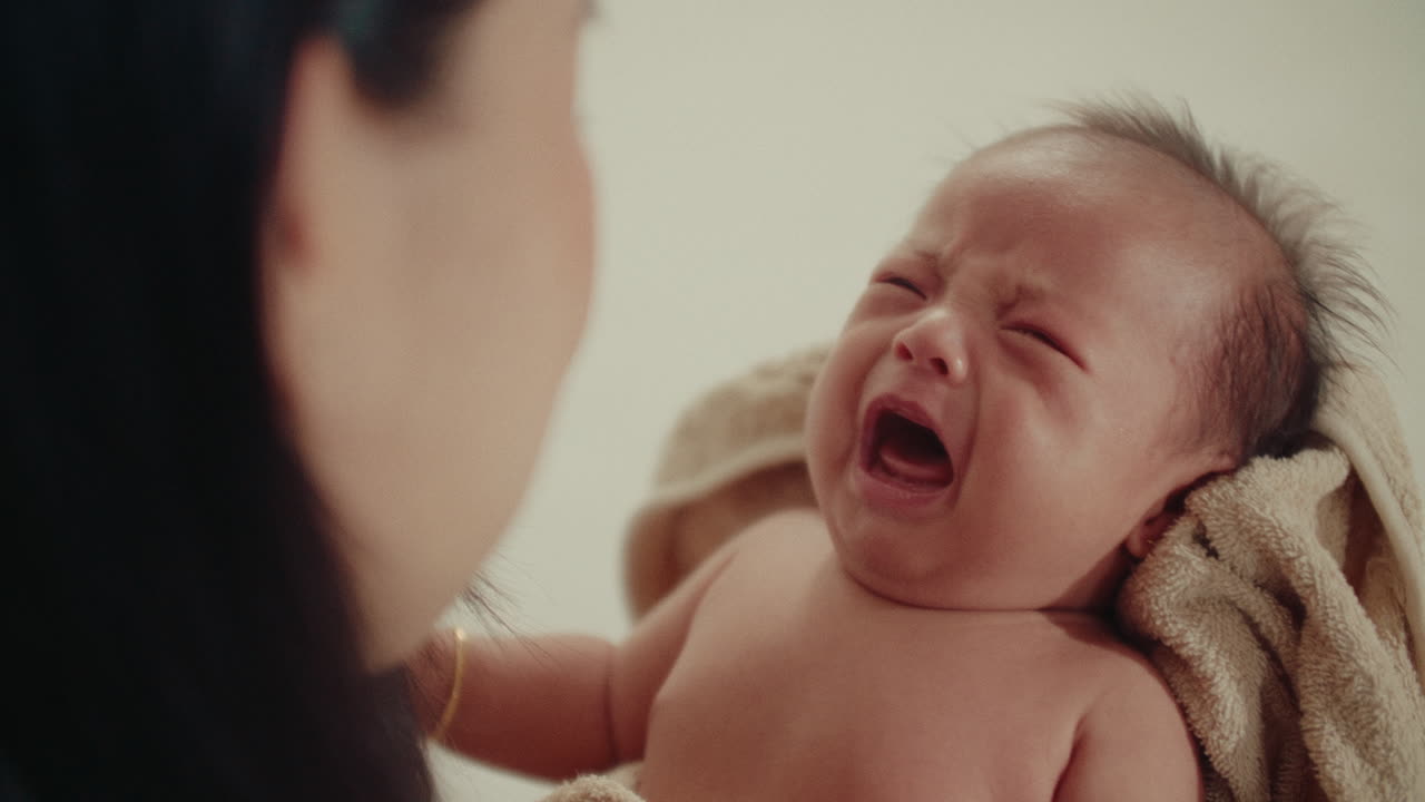 Mother Holding Newborn Baby Wrapped in Blankets, Over-the-Shoulder View of Infant Crying, cinematic light