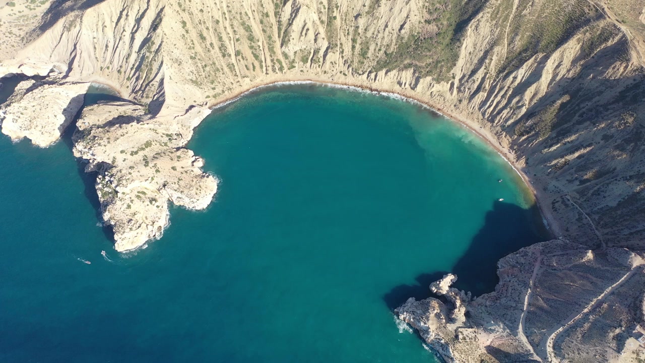 Prospettiva aerea elevata che mostra una spettacolare baia mediterranea semicircolare racchiusa da ripide scogliere montuose e acque cristalline color turchese in Marocco