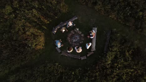 drone shot of mature friends making toast as they sit around fire at outdoor campsite