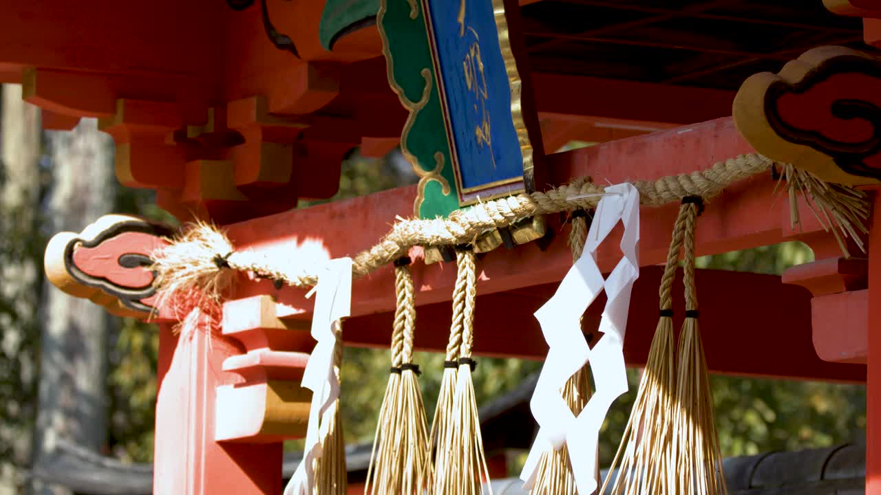 Camera zooms out from a vermilion Shinto shrine gate with traditional shimenawa rope