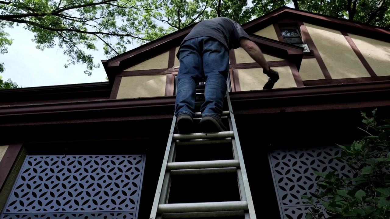 Man climbs ladder to clean his gutter of leaves and debris