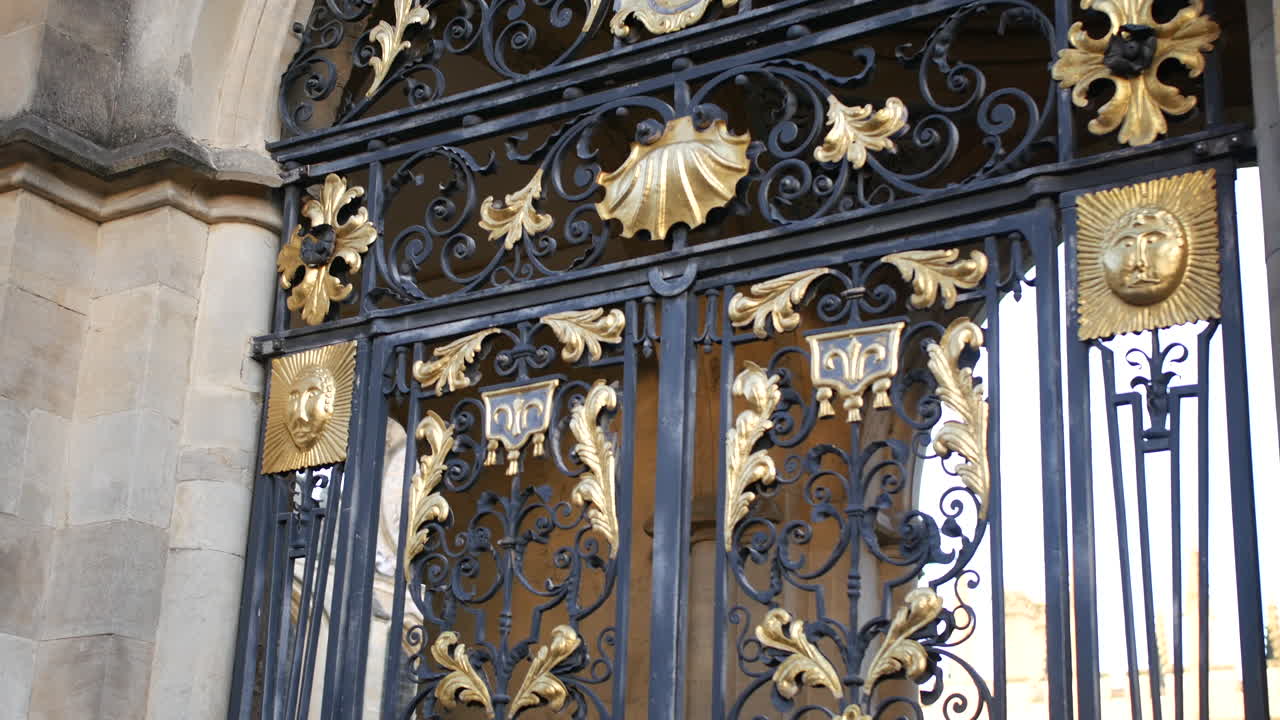 Portão de ferro preto luxuoso e ornamentado com ricos floreios dourados e brasão heráldico em arco de pedra - perfeito para passeios históricos, viagens de luxo ou branding de patrimônio europeu em turismo e estilo de vida