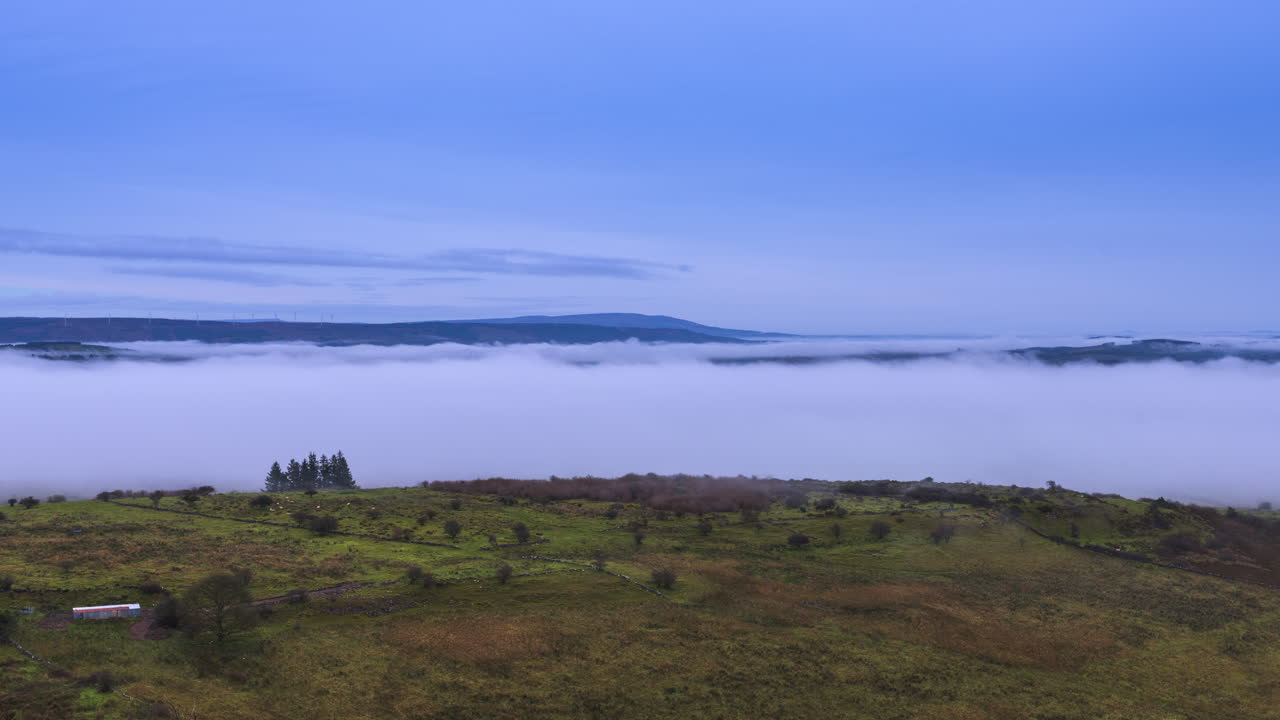 Zeitrafferaufnahme einer ländlichen Landschaft mit Nebelinversion, die über einem See in der Ferne und dahinterliegenden Hügeln rollt, gesehen von Carrowkeel im County Sligo in Irland.