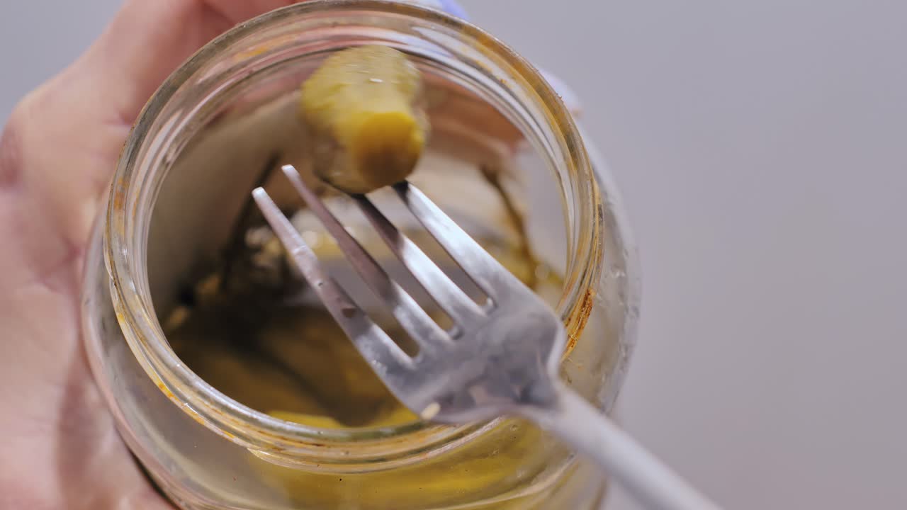 Fork reaches into jar of pickles with herbs visible in tangy brine close view