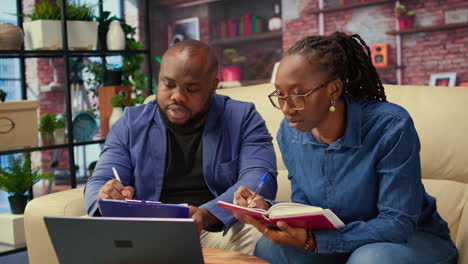 hombre y mujer negros escribiendo un informe con información del cuaderno