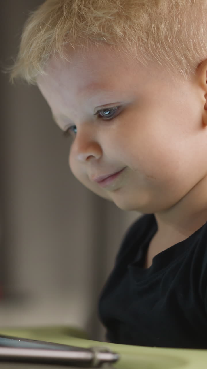 Happy little boy smiles watching funny cartoons via tablet at home closeup. Surprised toddler kid has fun with digital gadget. Internet technology