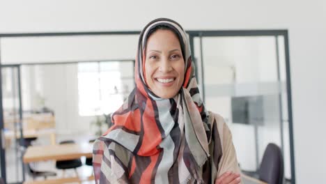 Portrait-of-happy-biracial-businesswoman-with-hijab-in-office-in-slow-motion