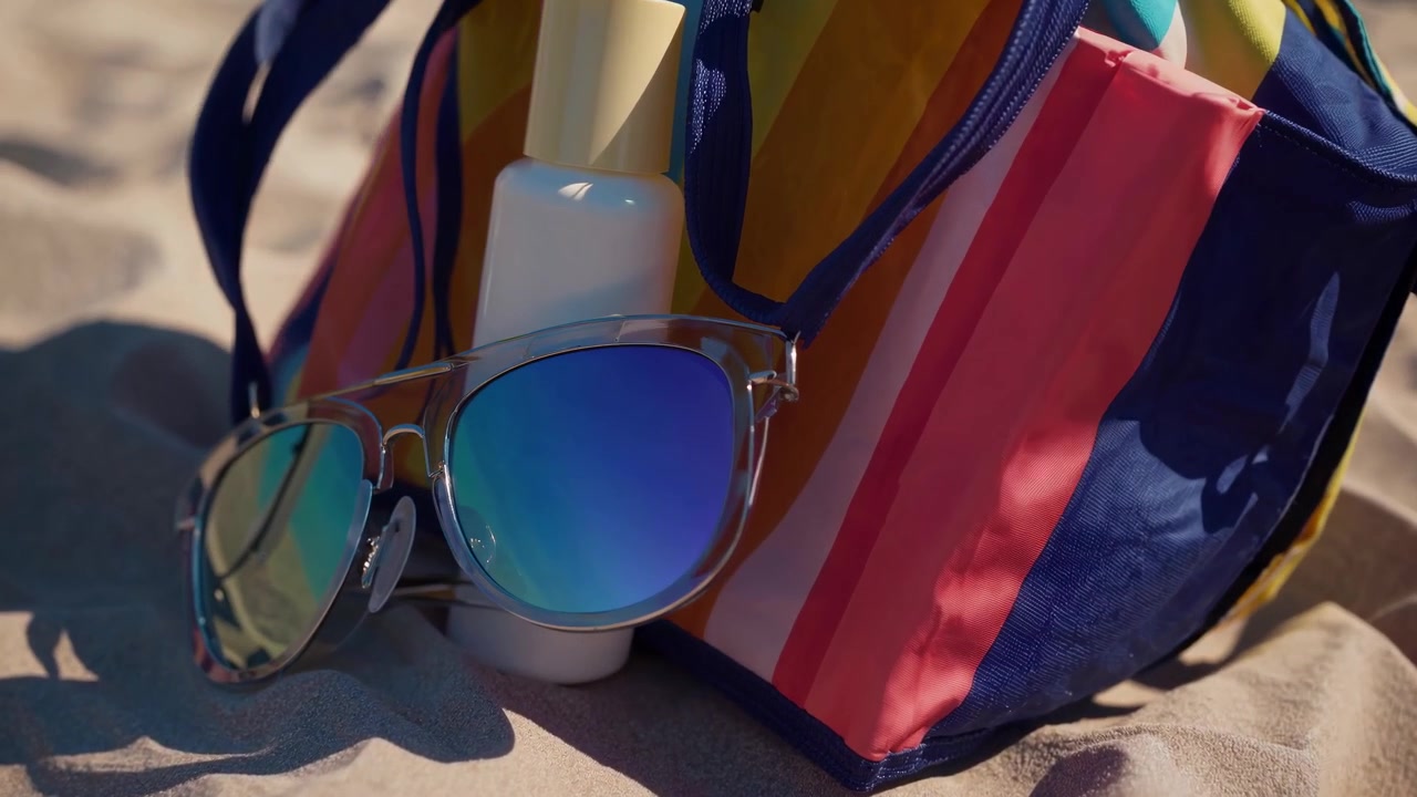 Fargerik strandveske med solbriller og solkrem på sandstrand