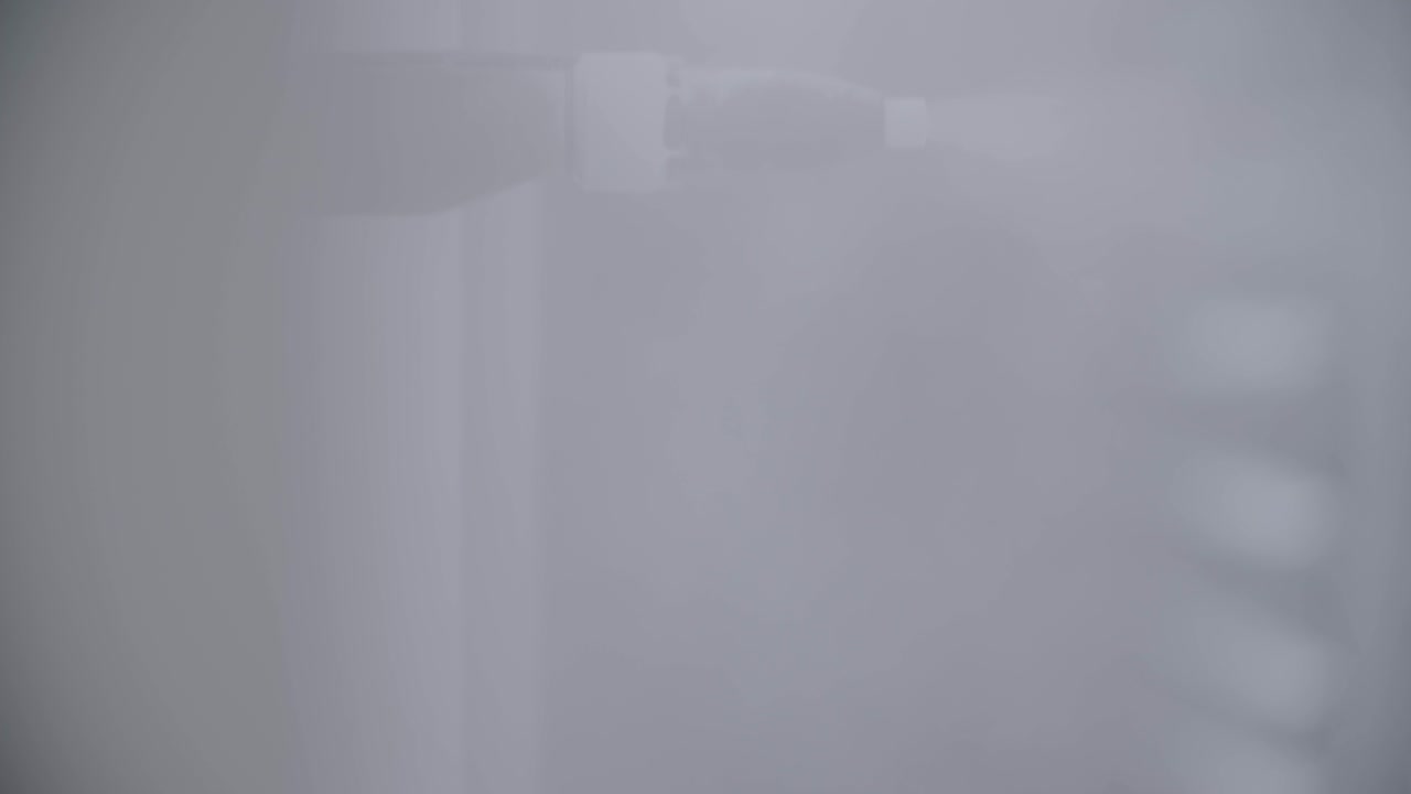 Primo piano di una macchina industriale che spruzza lentamente vapore trasparente su una superficie irriconoscibile, in una ripresa a mano in stile documentaristico.