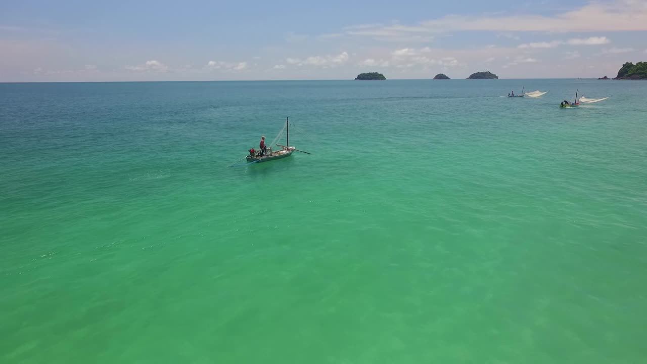 배경에 작은 섬이 있는 태국의 작은 나무 보트에 있는 전통적인 새우 어부의 공중 전방 돌리 샷