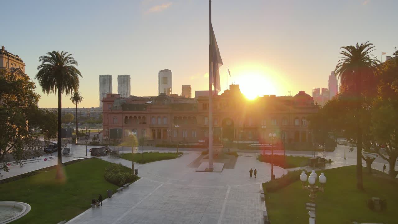 Aerial Drone Scene flying back of Casa Rosada, Buenos Aires, Argentina, the presidential pink house, the flag and the May Pyramid. Warm dawn morning sun backlight flare and reflections.