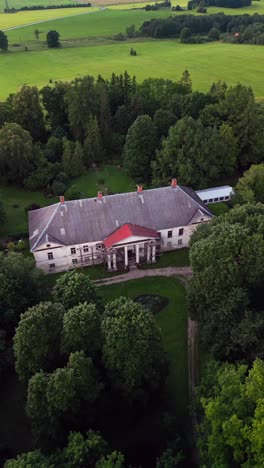 an aerial vertical video captures kirna manor in stunning detail with green fields gardens and peaceful countryside offering a glimpse of its historical elegance
