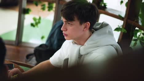 aerial view of youngster wearing white polo uttering words while looking away from camera, casual outdoor setting, sun flare on shoulders, expressive face, youth communication moment captured from above