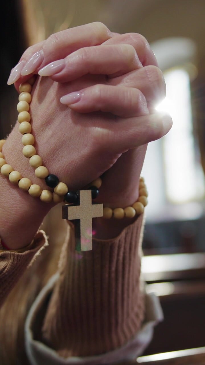 Donna seduta in silenziosa devozione, con le mani che tengono un rosario, che prega in un banco di chiesa di legno durante.