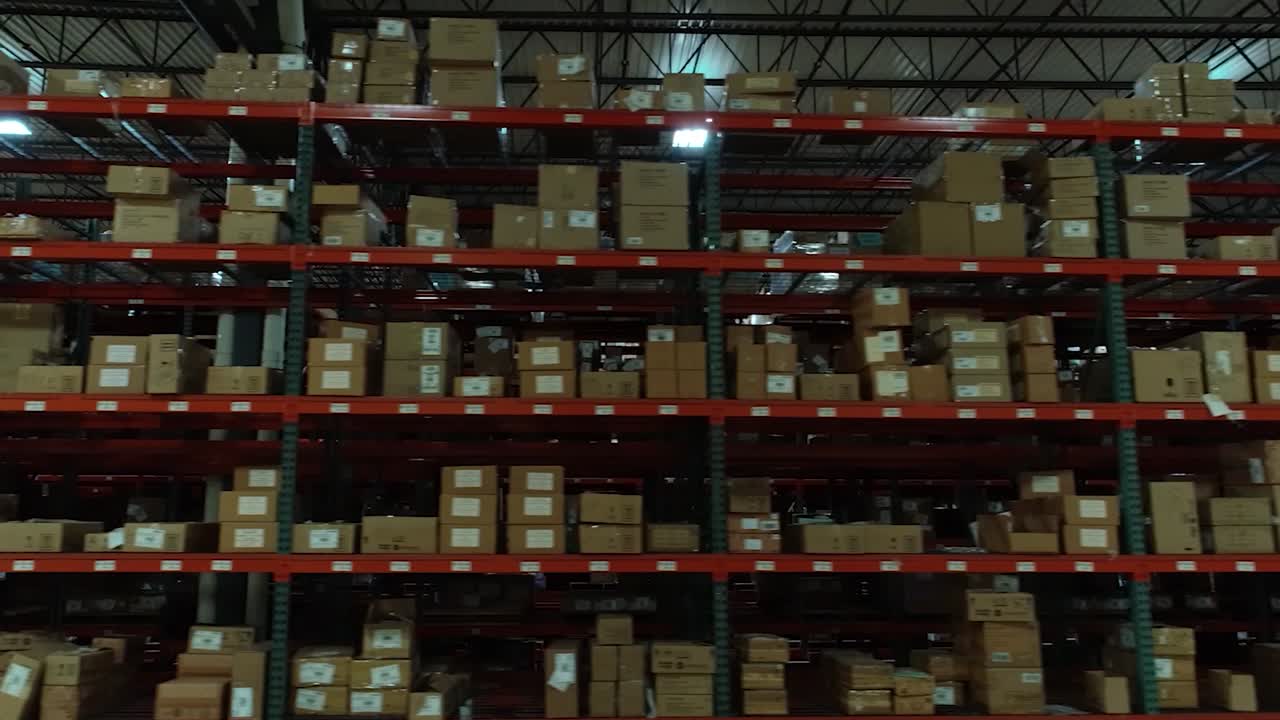 A smooth lateral drone shot moving left at a constant altitude, passing tall warehouse shelves filled with neatly stacked boxes