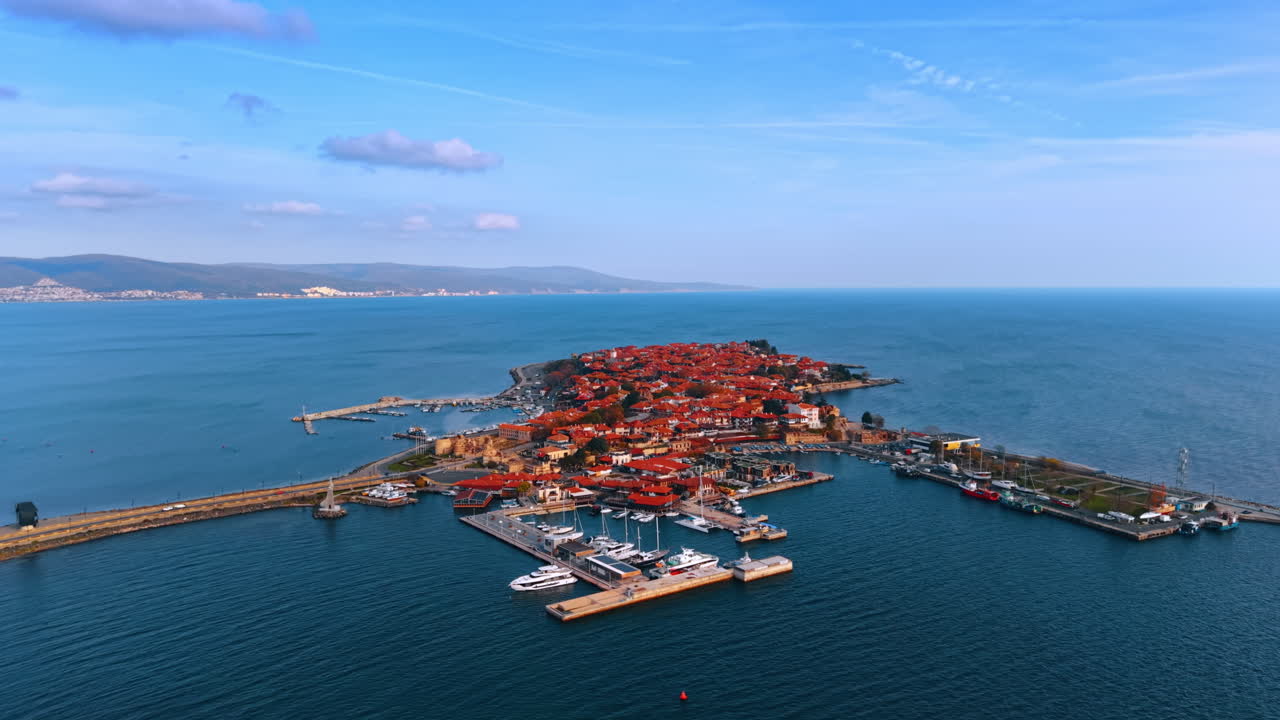 Historisk östad med röda tak och marina faciliteter. Flygfoto över en gammal stad belägen på en ö förbunden med en bro, med en marina och båtar.