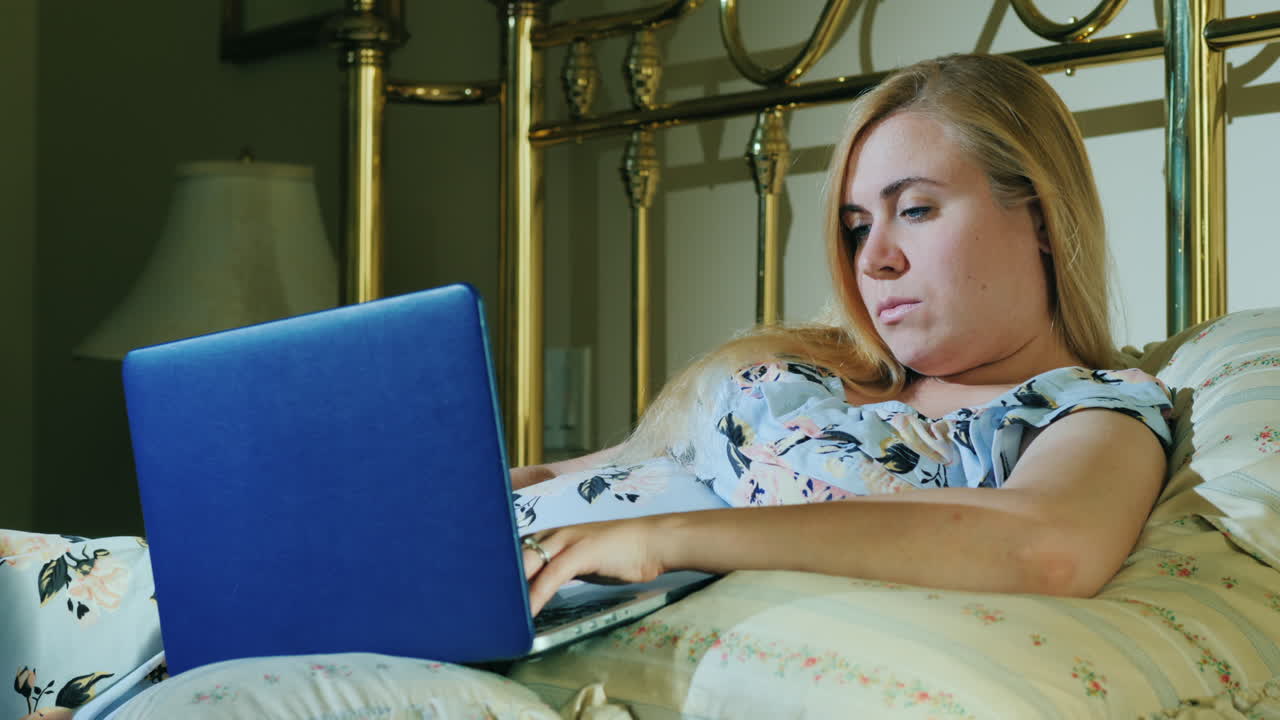 Young Woman With Laptop Resting In Bed In Her Bedroom