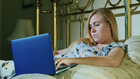 Young-Woman-With-Laptop-Resting-In-Bed-In-Her-Bedroom