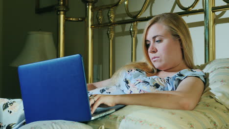 young woman with laptop resting in bed in her bedroom