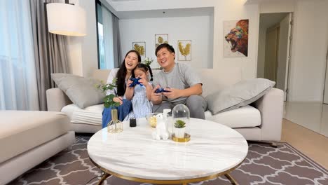 A family enjoys playing video games together on a sofa in a well-lit, modern living room
