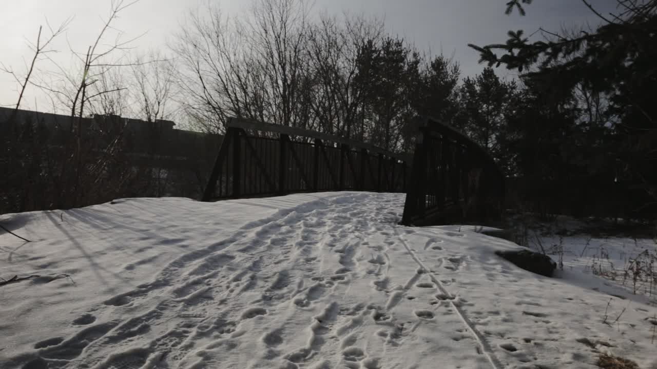 Footprints On The Thick White Snow Covering The Footbridge With Bare Trees In Winter - Panning Shot