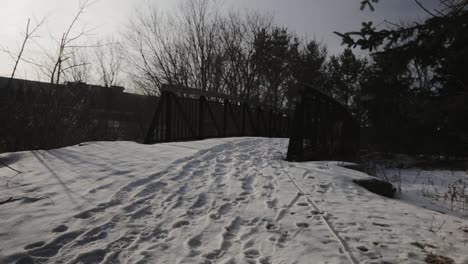 footprints on the thick white snow covering the footbridge with bare trees in winter - panning shot