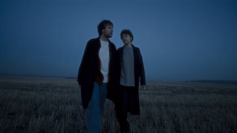 couple walking hand in hand across open field at dusk