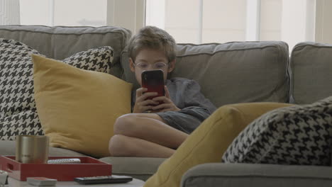 cute boy snuggled up on the couch plays around on his smartphone