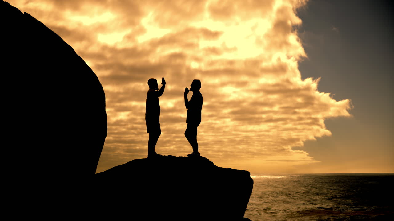 Two people celebrating on a cliff at sunset
