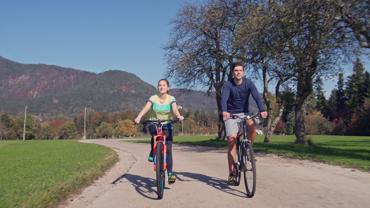 Mujer y hombre andando en bicicleta y disfrutando de la naturaleza en un día soleado de otoño, vista frontal.
