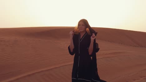 mujer musulmana de pie cerca de la mezquita en el desierto. viento fuerte oriente medio paz sin guerra