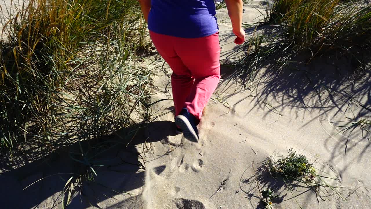 La donna corre sulle dune sabbiose verso il mare. Movimento rallentato